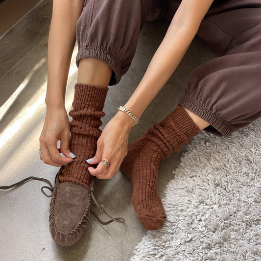 Person wearing brown ribbed socks and brown moccasin shoes on a light gray surface.