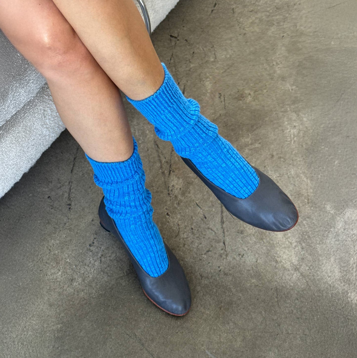 Person wearing bright blue socks with dark shoes on a concrete floor.