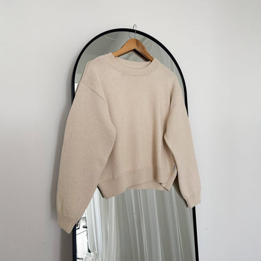 A naturel cotton sweater on a hanger in front of a mirror against a white wall