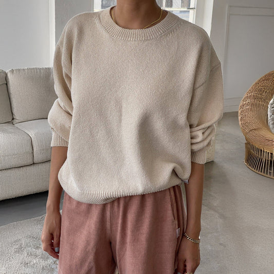 A person wearing a naturel sweater and pink pants in a neutral living room setting
