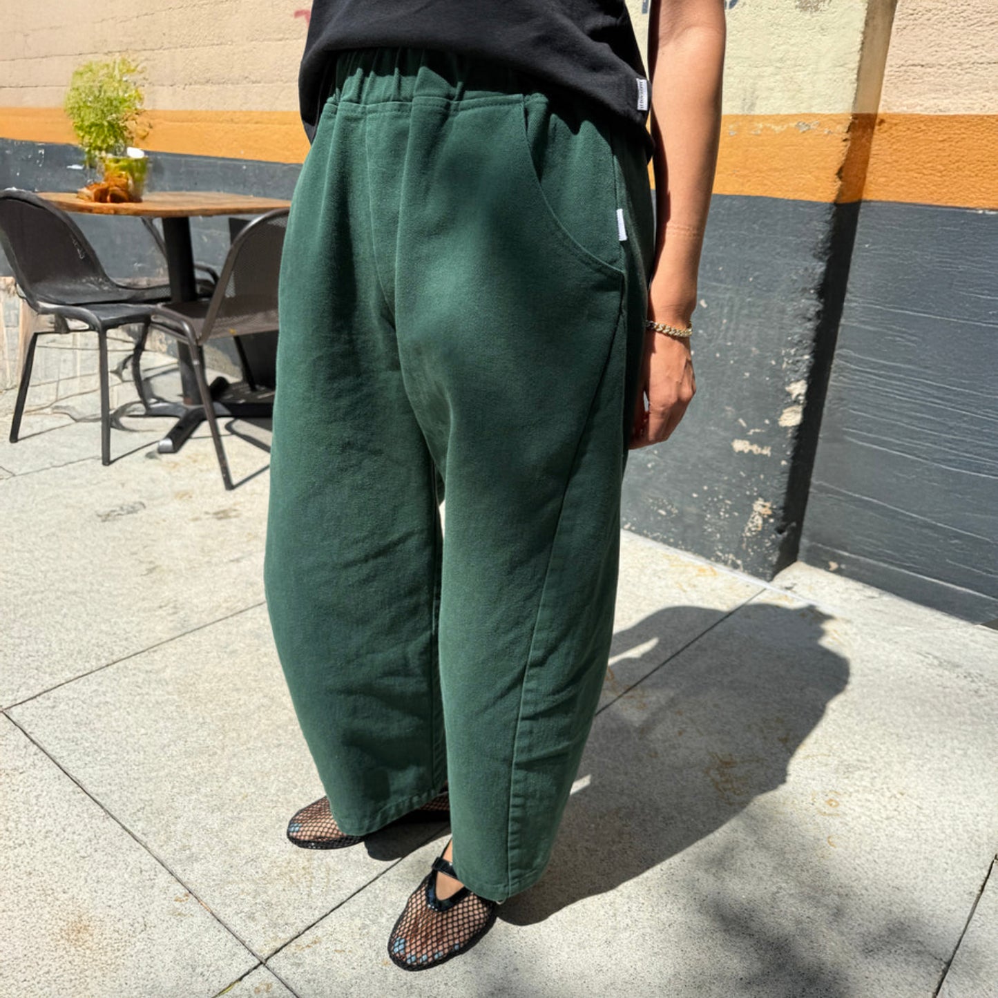 Person wearing green pants standing outdoors on a sidewalk.