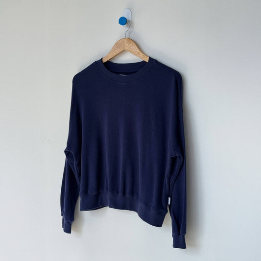 Navy blue sweatshirt on a wooden hanger against a white wall