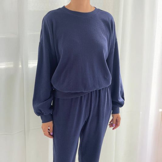 Person wearing a navy blue sweatshirt and pants set against a white curtain background