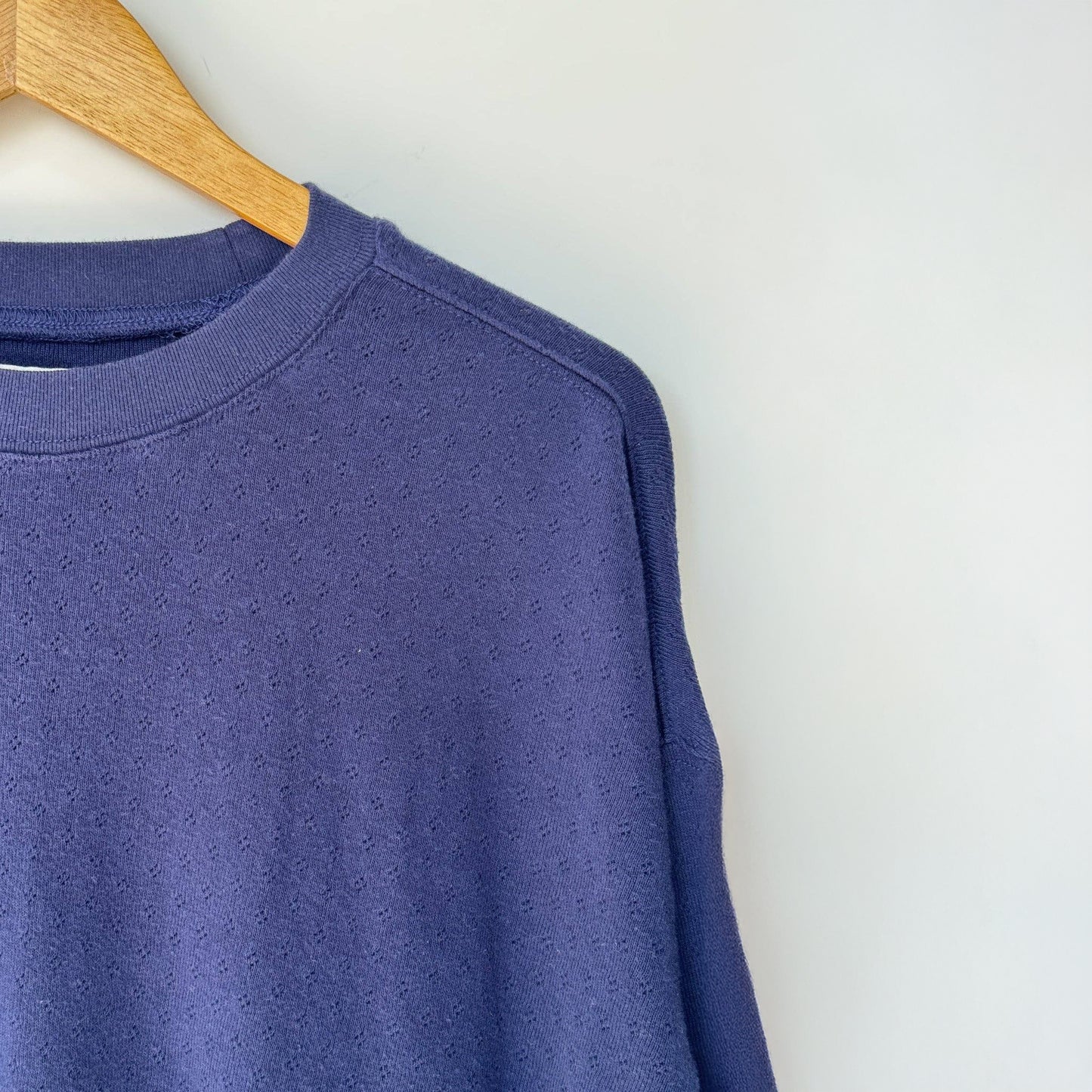 Blue sweatshirt on a wooden hanger against a white background