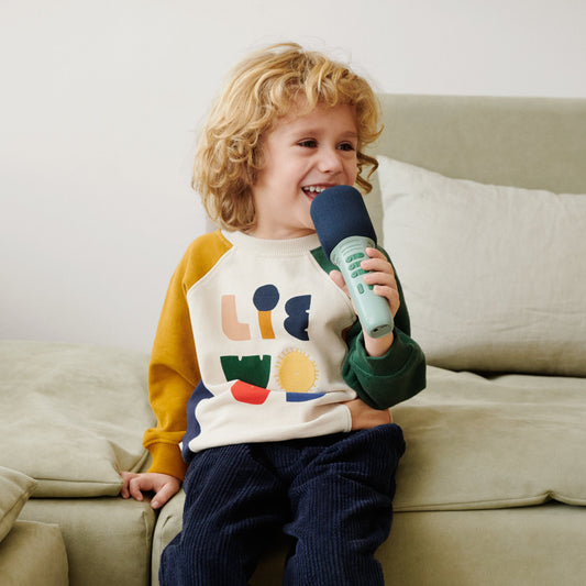 Child sitting on a couch holding a microphone with a colorful sweater