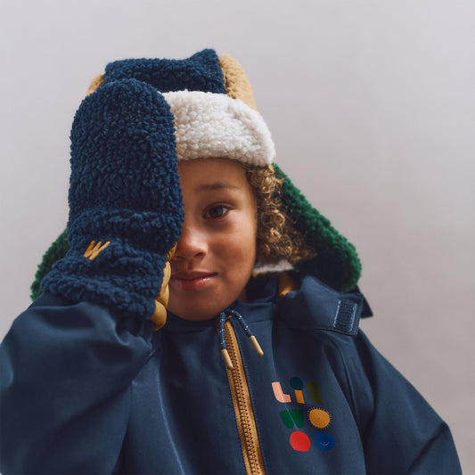 Child wearing a blue jacket with colorful designs and a matching hat and gloves on a plain background