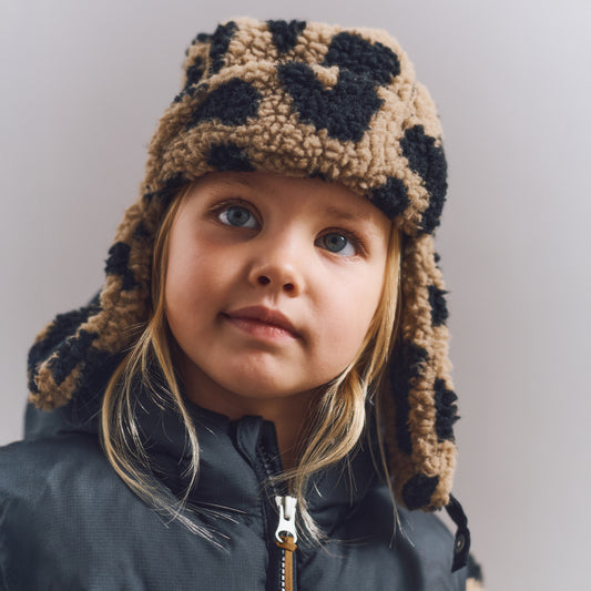 Child wearing a leopard print hat and dark jacket against a plain background