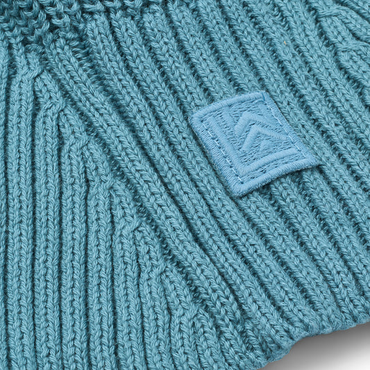 Close-up of a teal knitted balaclava with a logo patch.