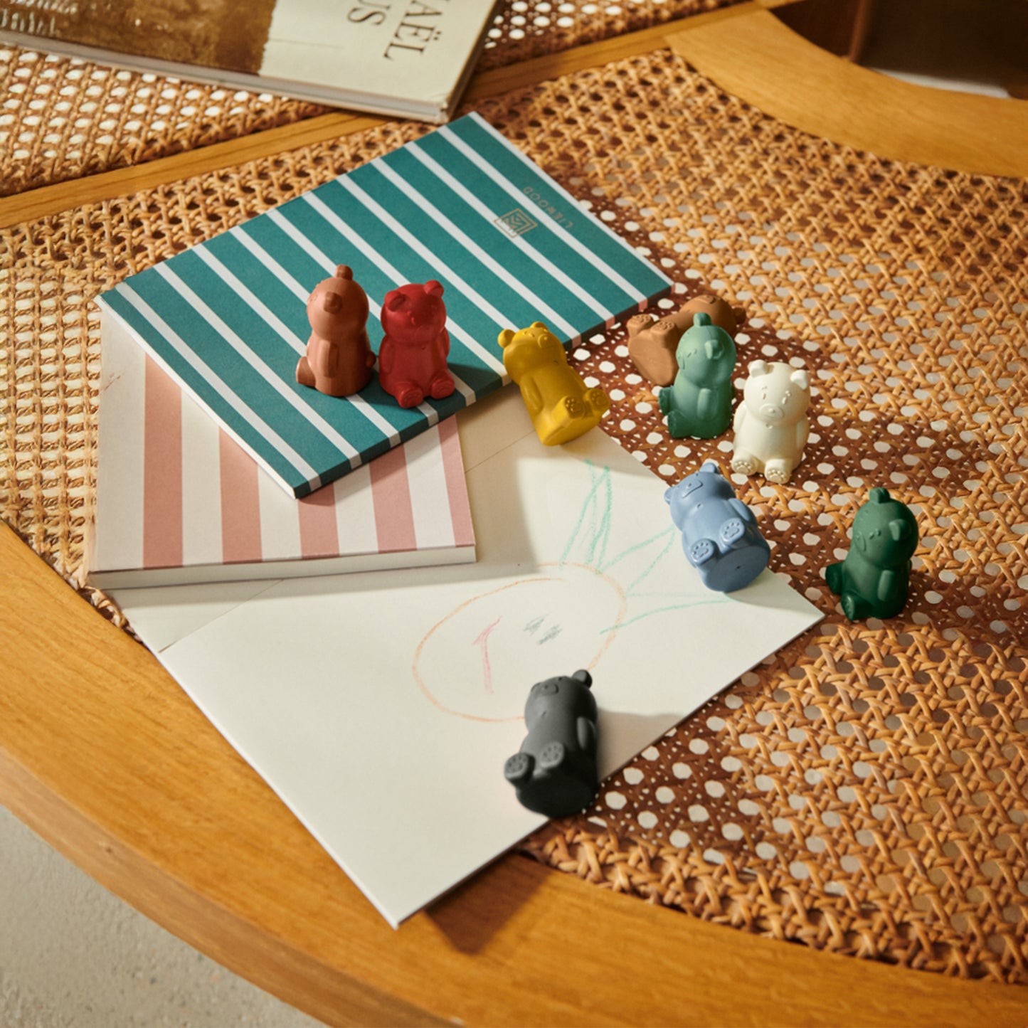 Colorful animal crayons on a striped notebook with drawings on a wicker table top