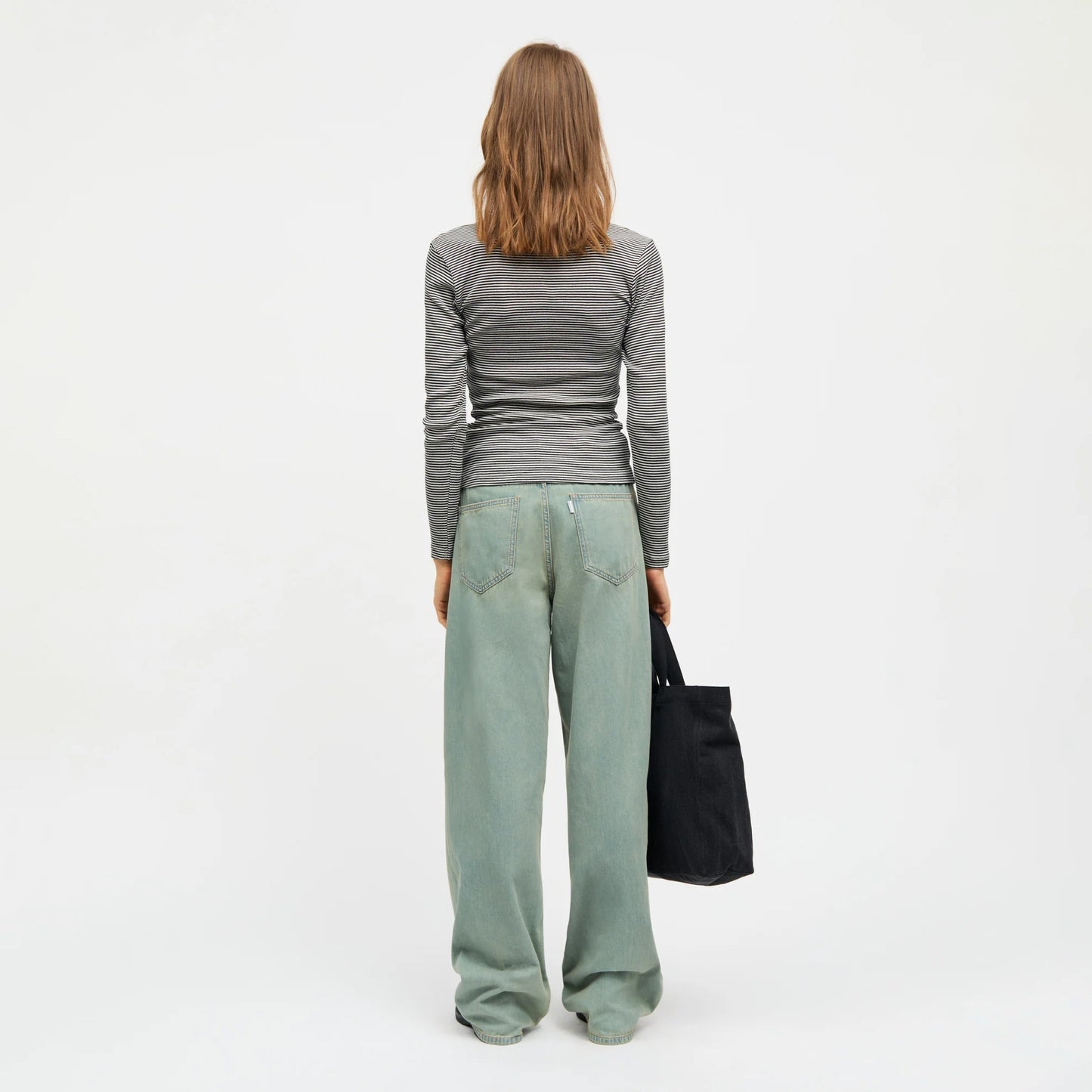Person wearing a gray long-sleeve top and light blue jeans on a white background. The view is from behind.