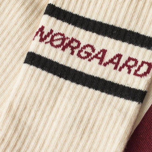 Close-up of an off white sock with 'Norgaard' branding on a textured background