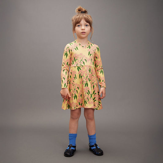 Young girl wearing a floral dress, blue socks and black shoes against a gray background