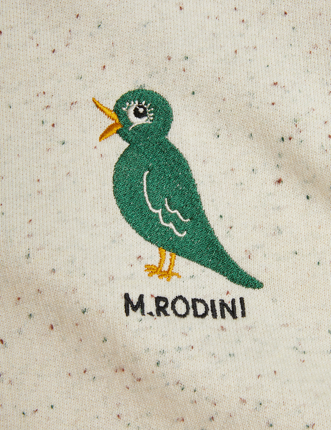 Embroidered green bird design on a textured beige fabric with 'M.Rodini' branding.