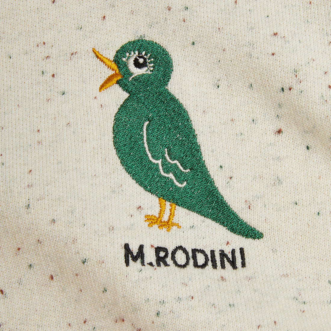 Embroidered green bird design on a textured fabric with 'M.Rodini' branding.