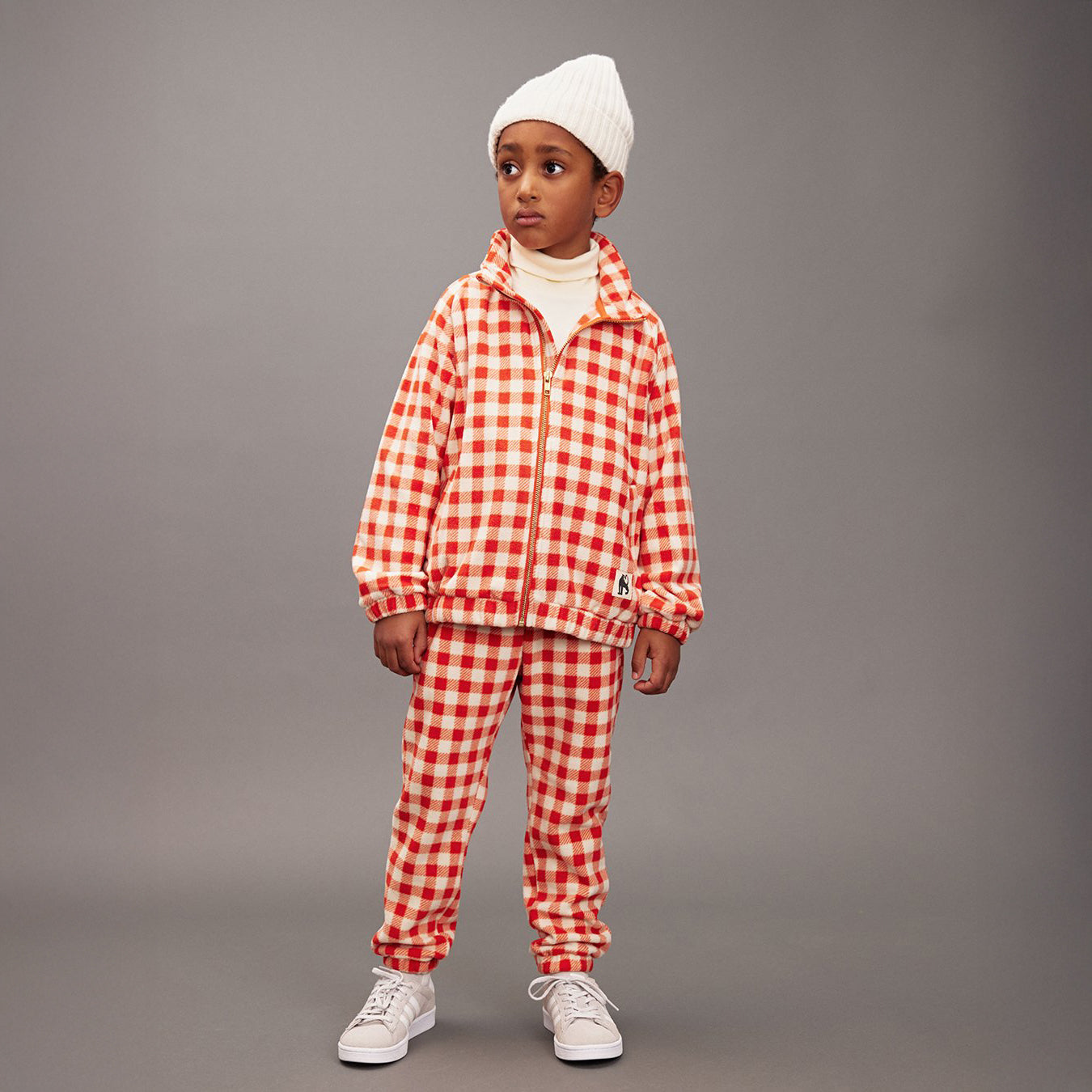 Child wearing a red and white checkered outfit with a gray background