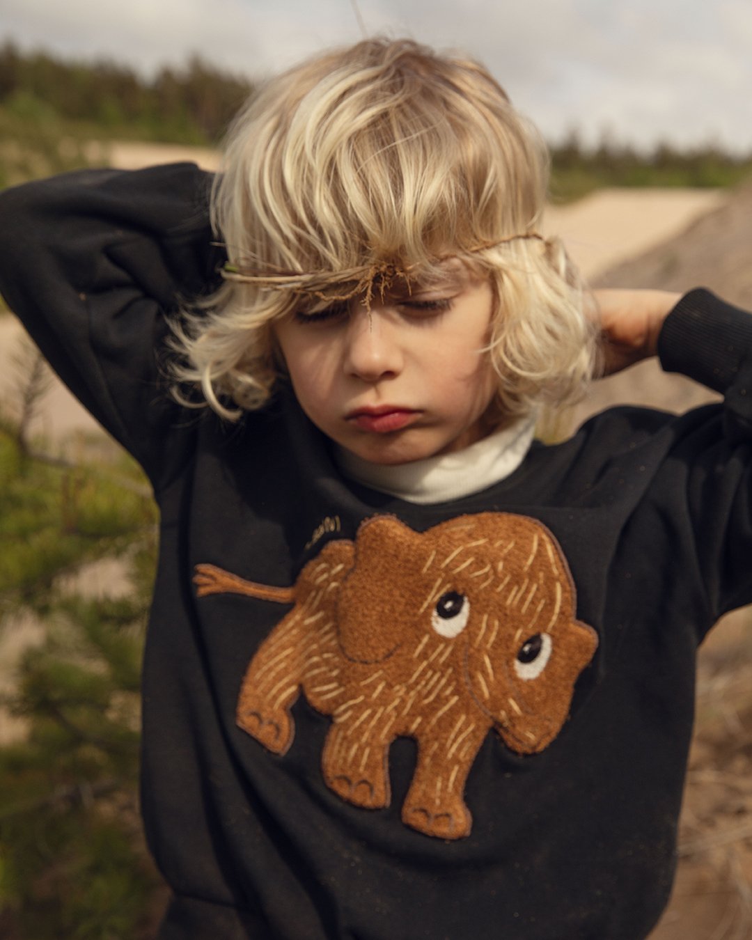 Child wearing a black sweatshirt with a brown mammoth design outdoors