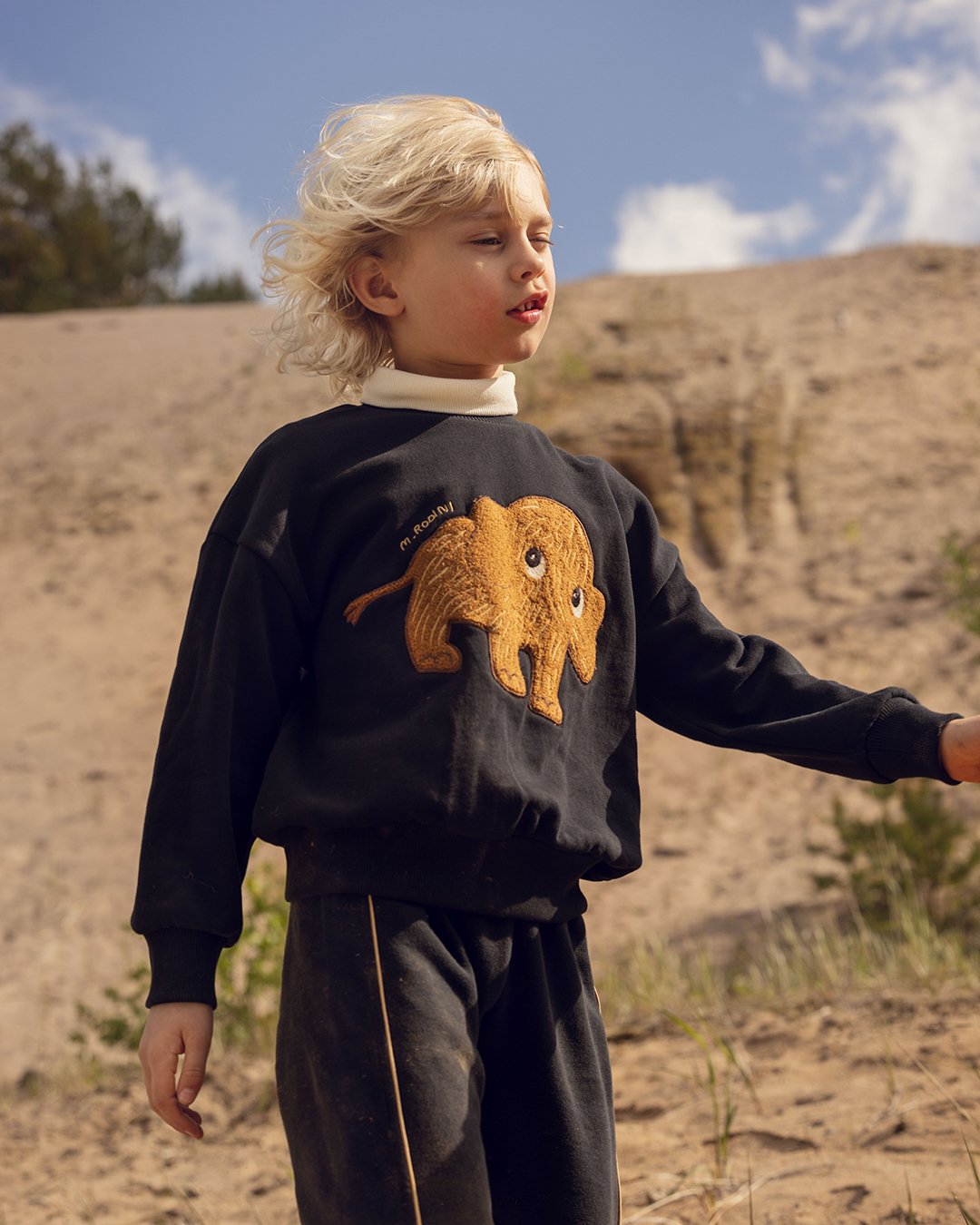 Child wearing a black sweatshirt with a mammoth design in a desert setting