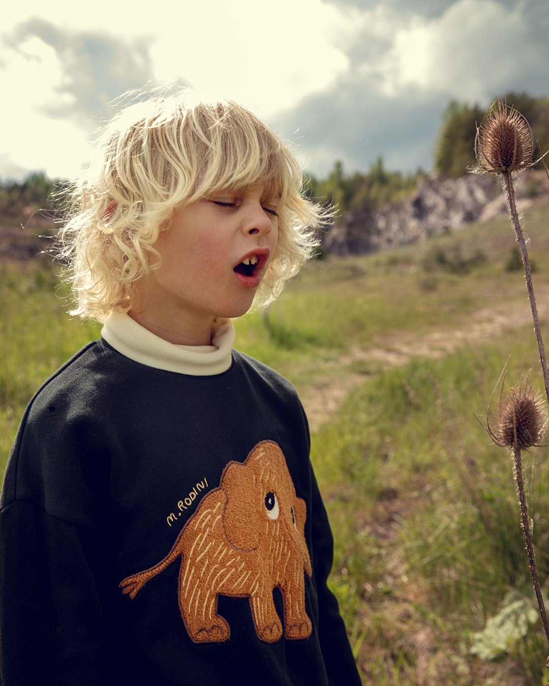 Child wearing a black sweater with an elephant design in a natural setting