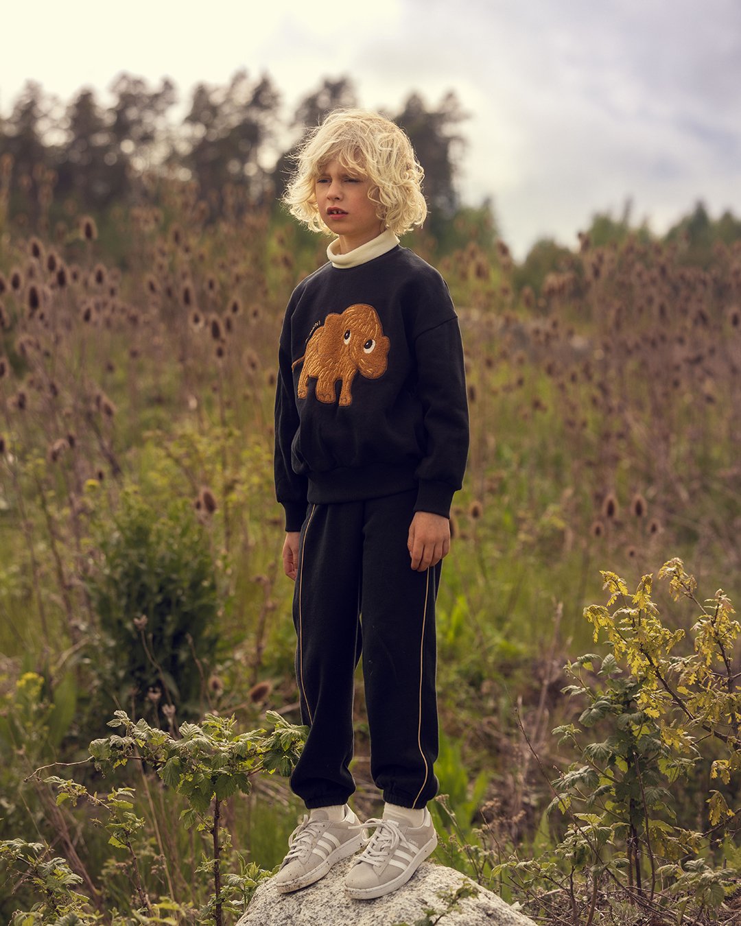 Child wearing a black sweater with a mammoth design in a natural setting