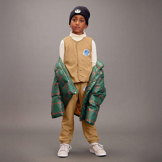 Child wearing a green plaid coat over a beige outfit on a gray background