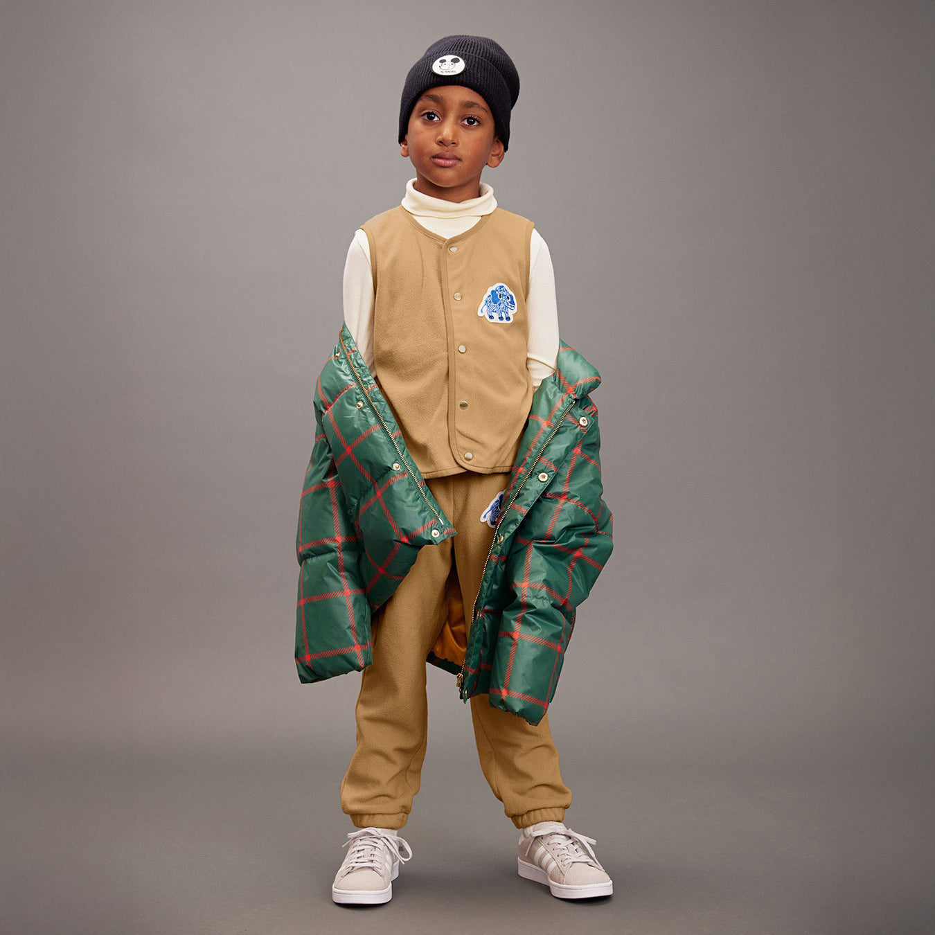 Child wearing a beige vest, plaid jacket, and pants on a gray background