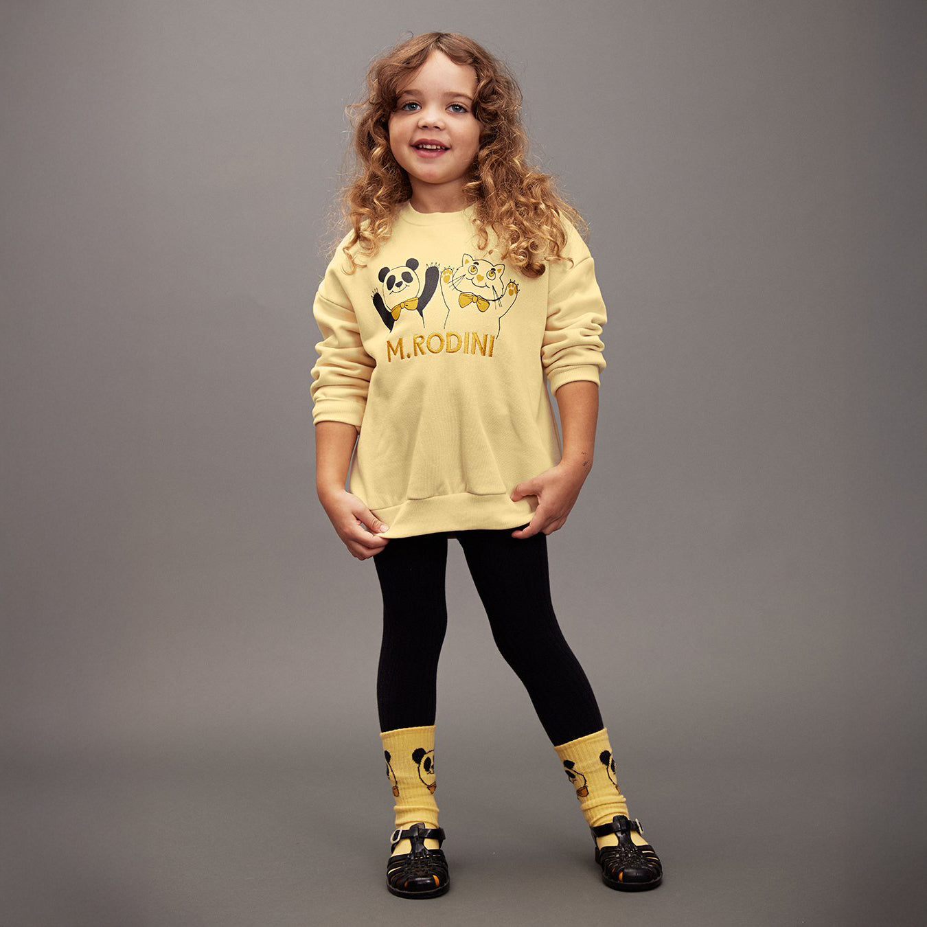 Child wearing a yellow sweater with cartoon characters and text on a gray background