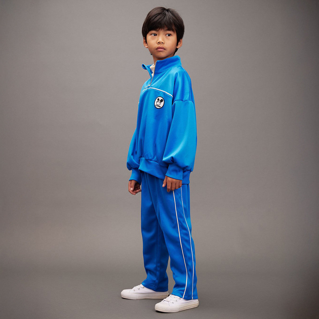 Child wearing a blue tracksuit with a logo on a gray background