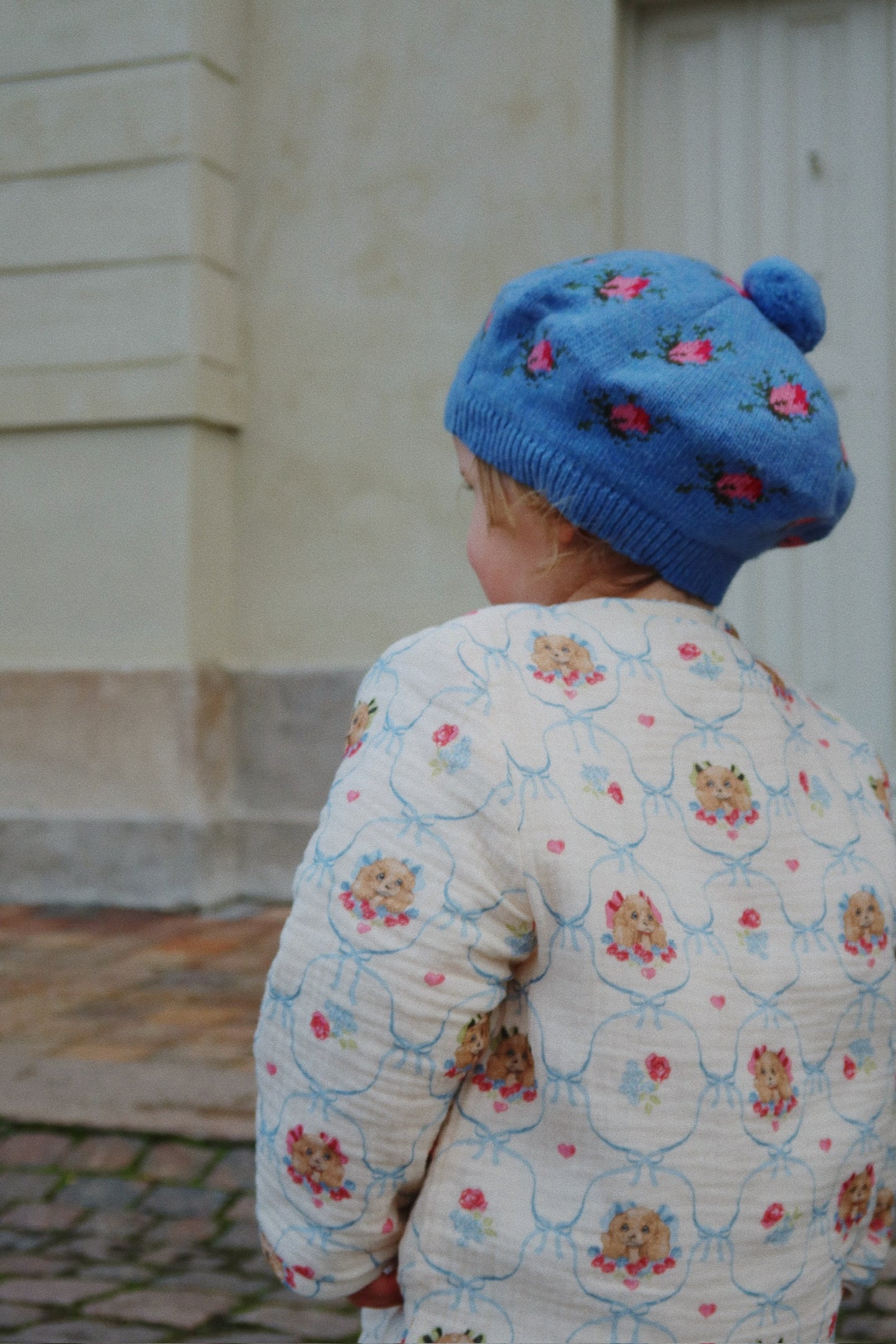 Child wearing a blue knitted hat with floral patterns, standing outdoors.