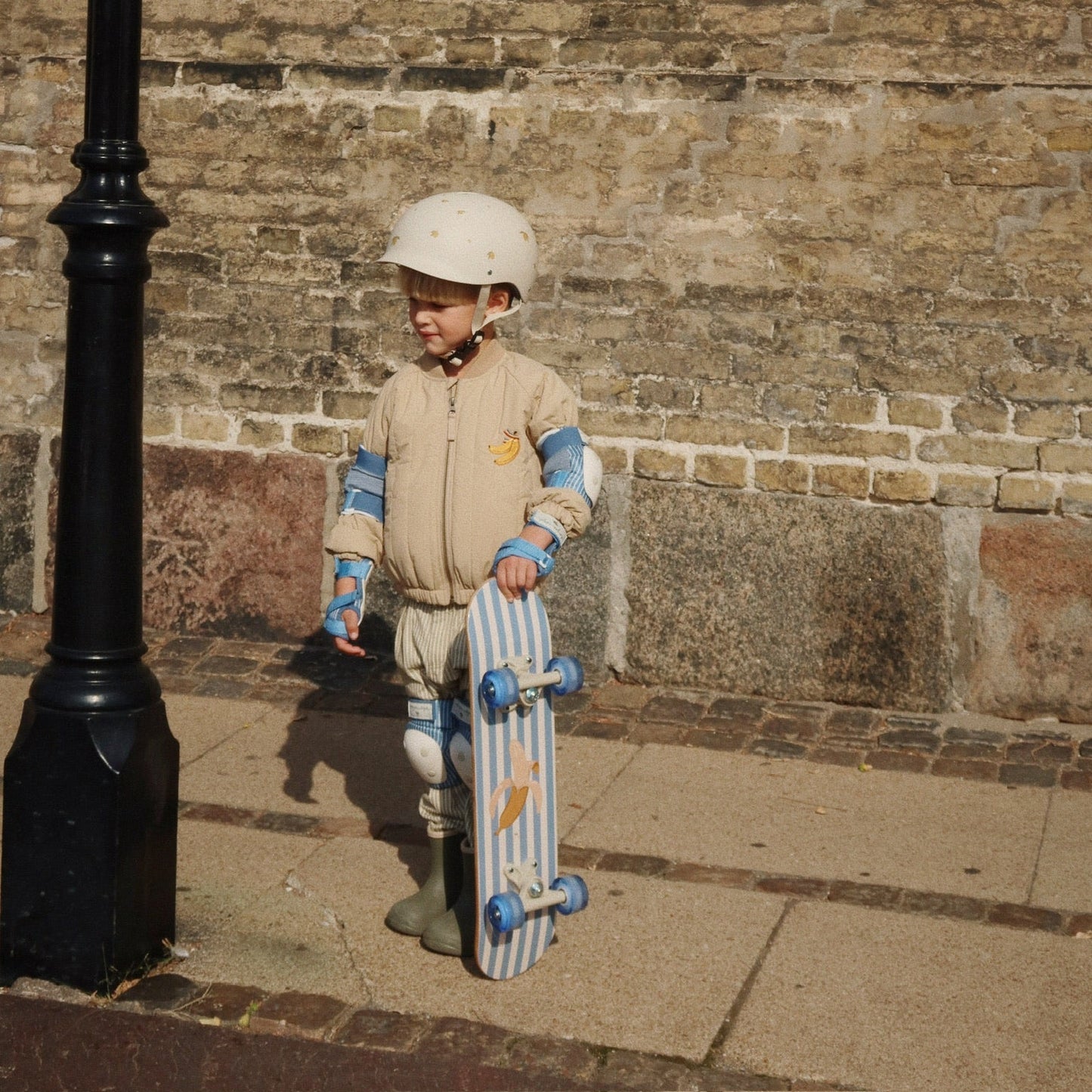 Child holding a skateboard against a brick wall