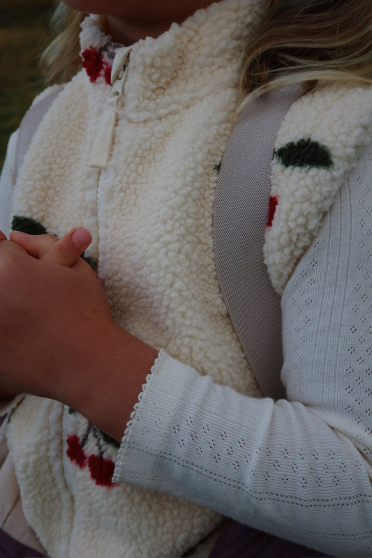 Close-up of a person wearing a white sweater with a patterned vest over it.