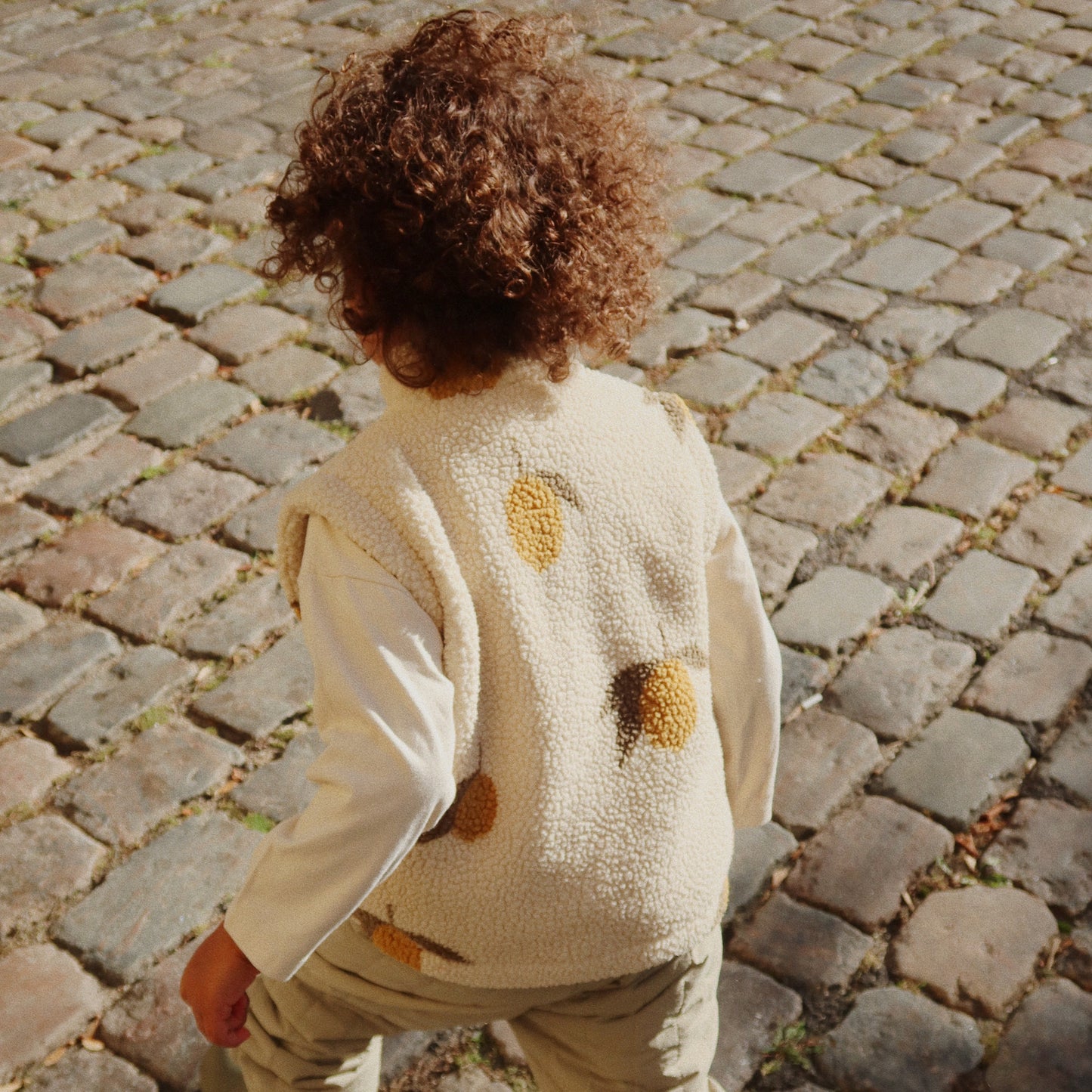 Person wearing a beige sweater with brown polka dots on a cobblestone street