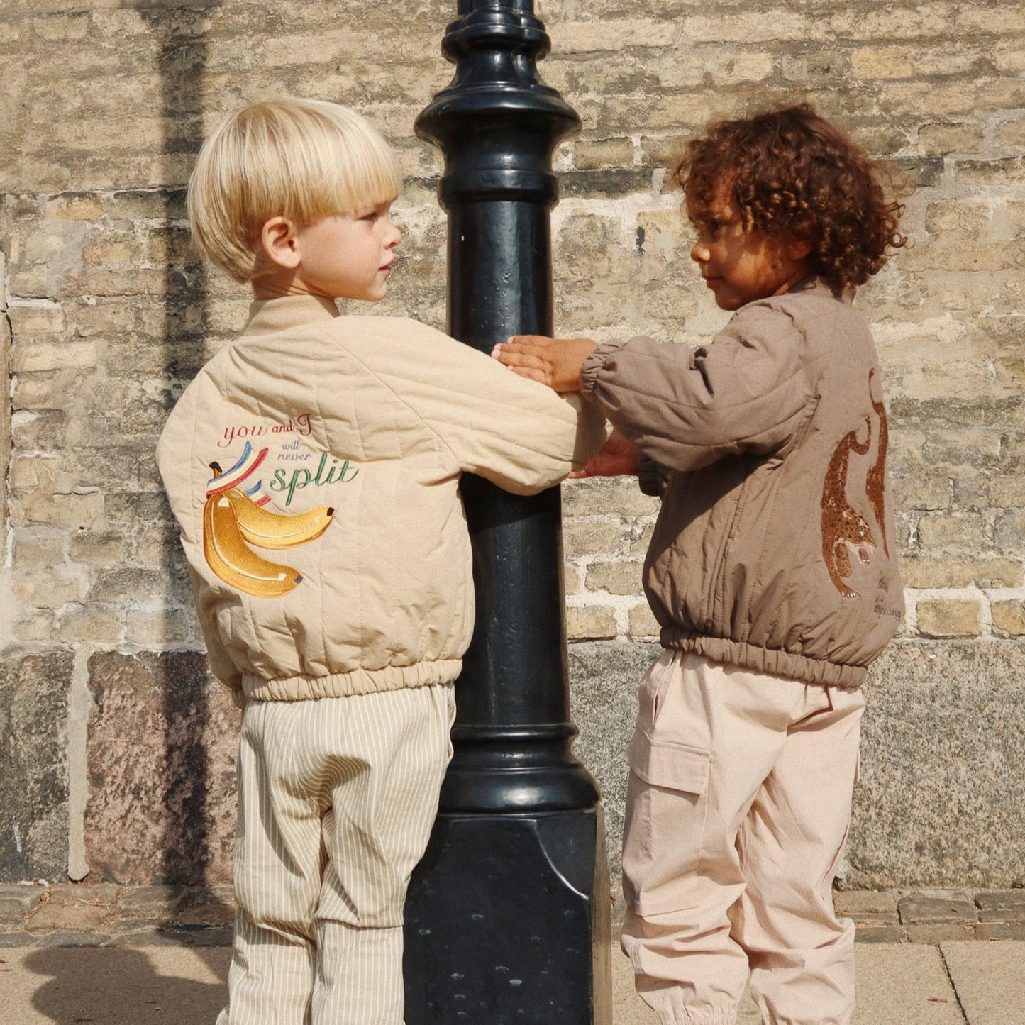 Two children in coordinated outfits standing next to a black lamp post against a stone wall.