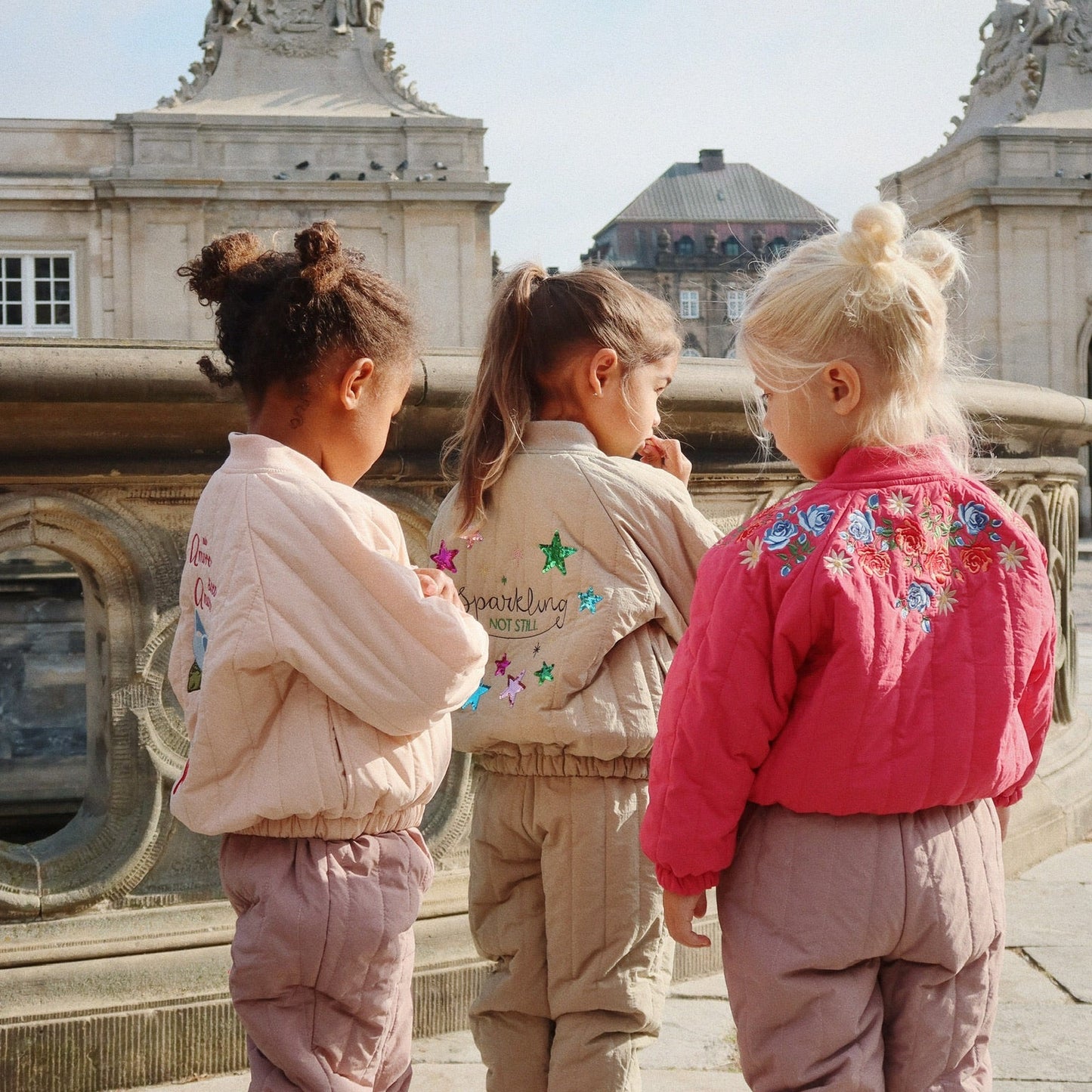 Three children in matching outfits standing in front of a historic building.