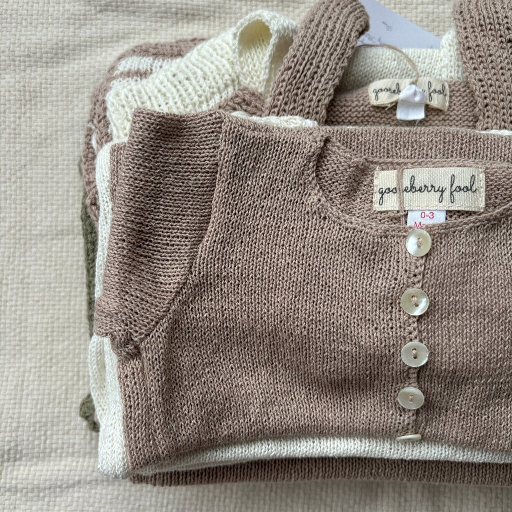 Stack of baby sweaters with a visible brand label on a textured surface