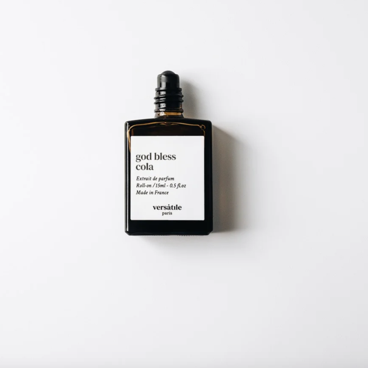 An image of a brown perfume bottle without the lid on it. The bottle has a square white label on it that says the scent of the perfume 'god bless cola' along with the amount of perfume in the bottle, that being 15ml and where the perfume was made, that being in France. Beneath this it says versatile Paris.