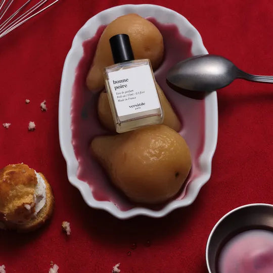 Perfume bottle labeled 'bonne poire' on a plate with pears on a red background