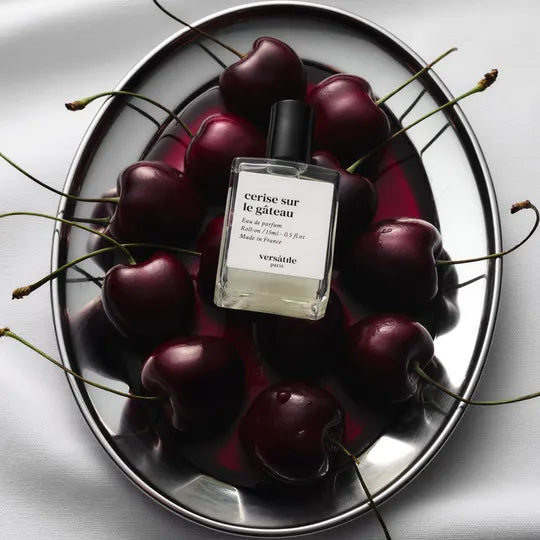 Versace perfume bottle surrounded by cherries on a reflective surface