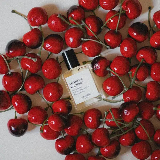 Versace perfume bottle surrounded by red cherries on a light background