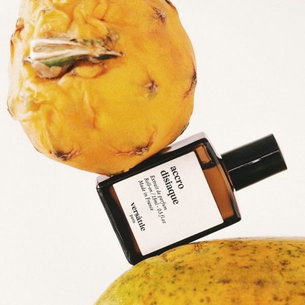 Perfume bottle labeled 'accro discorde' next to a pineapple on a white background