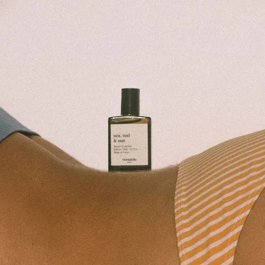 Perfume bottle labeled 'sea, sand & sun' by 'versatile' on a textured surface.