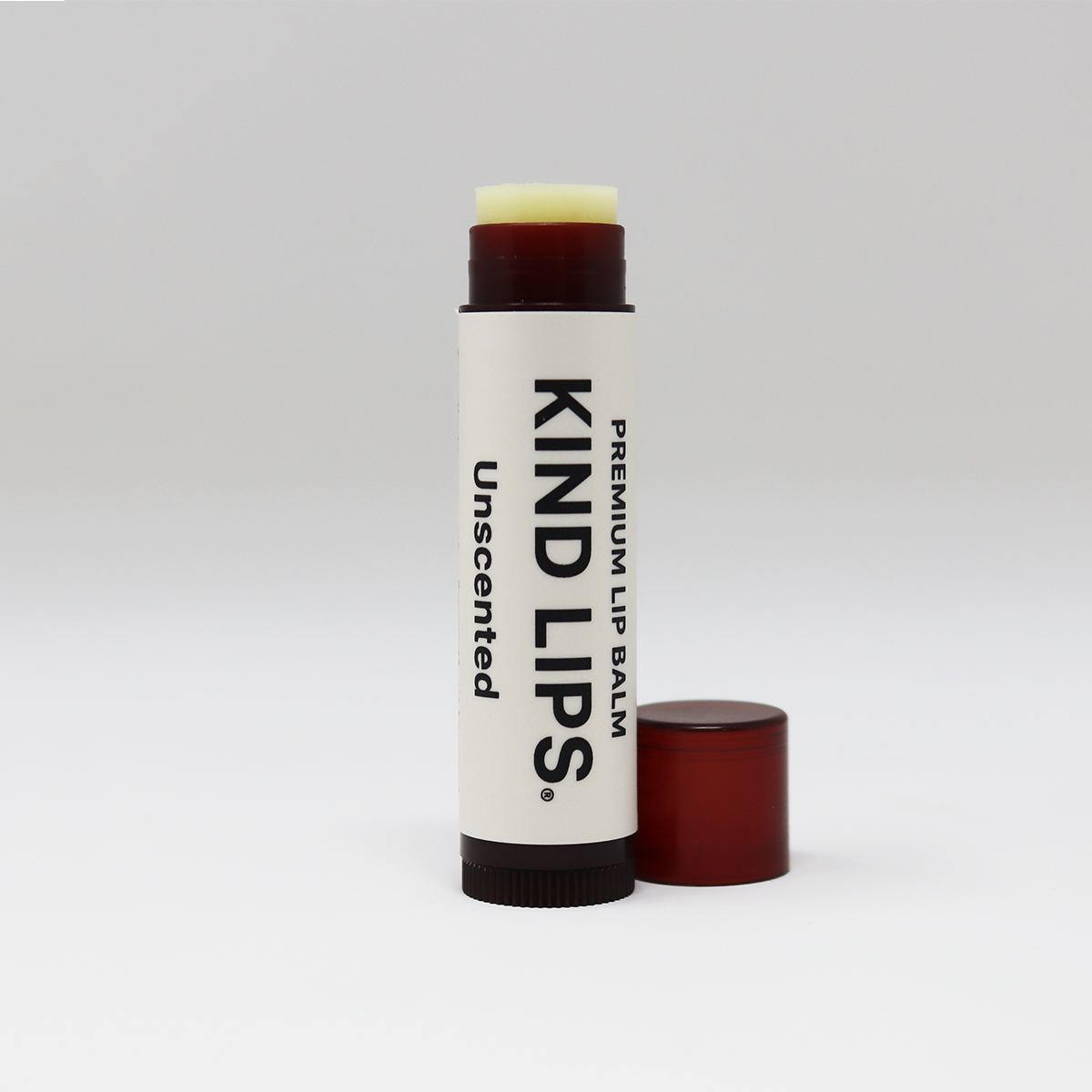 A stick of unscented lip balm with the brand name 'Kind Lips' displayed on it, with the cap removed, showing the balm stick.