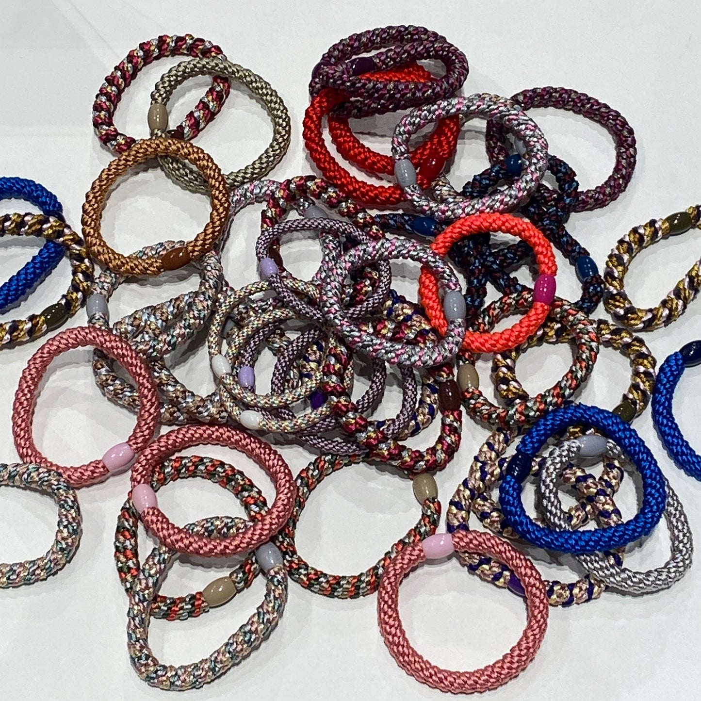 A collection of Bon Dep Kknekki hair ties in various vibrant colours, featuring a unique woven design and soft, elastic texture. The hair ties are displayed in a mix of bright, pastel, and neutral tones, showcasing their versatility and stylish appeal.