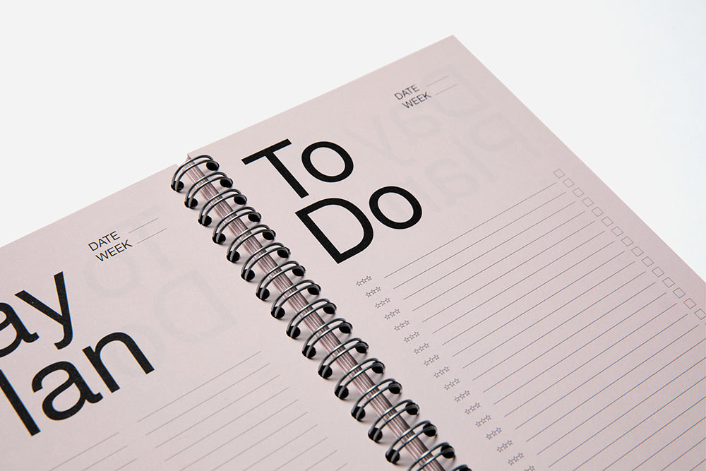 An open washed Pink spiral binder planner with the text - Day Plan and To Do written on the pages, placed on a white background.