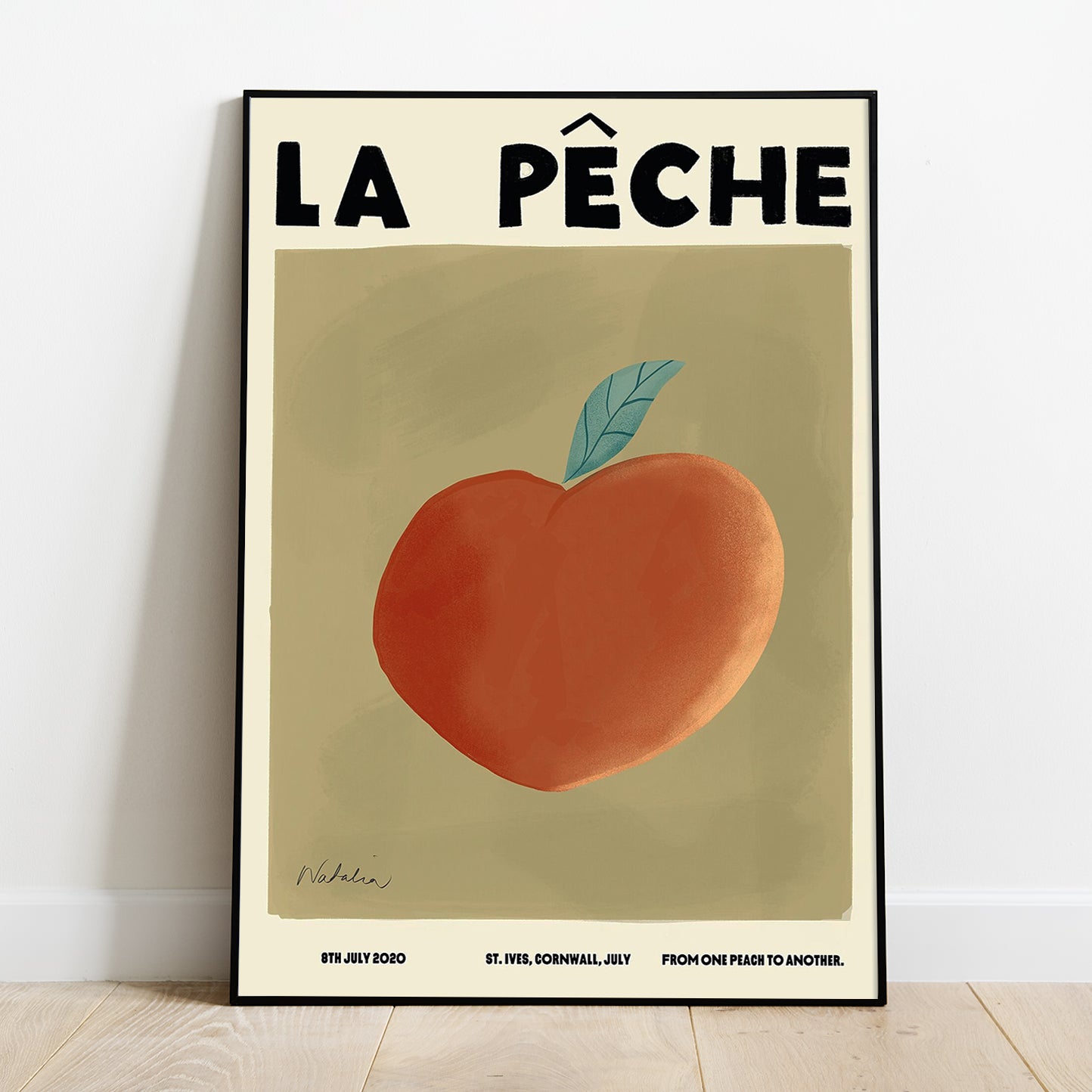 A Natalia Bagniewska Peach Print. The print has an olive green background. It says “La pêche” which means the peach in French. The peach is orange peachy in colour. The leaf is green. Beneath the olive green background in black, on the left hand side it says 8th July 2020, in the middle it says St.Ives, Cornwall, July and on the right it says From One Peach To Another. The print is framed and kept against a white wall on a wooden floor.