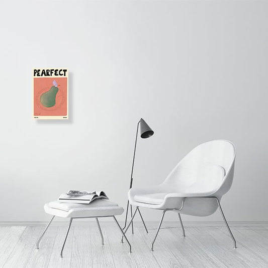 A Natalia Bagniewska Pearfect print in a drawing room setting. In this print,the background is peachy pink in colour. The pear is green in colour with the leaf being lilac. It is kept on a transparent plate. The print is framed and hung on a white wall over a wooden floor. The chair, stool and floor are all white.
