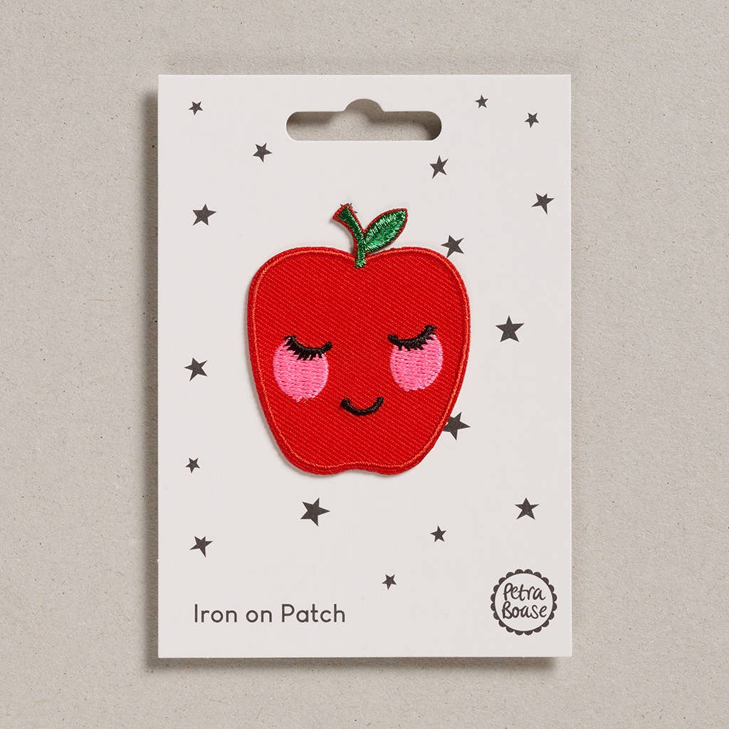 an embroidered red apple with pink cheeks, brown stem and green leaf. The background is white with black stars