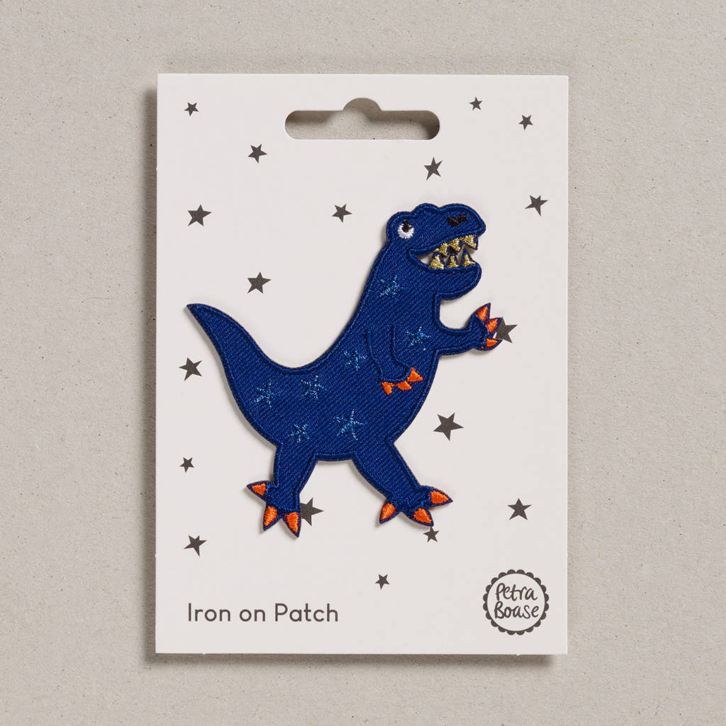 an embroidered dark blue dinosaur with light blue scales. The dinosaur has orange claws, golden teeth and black eyes. The background is white with black stars