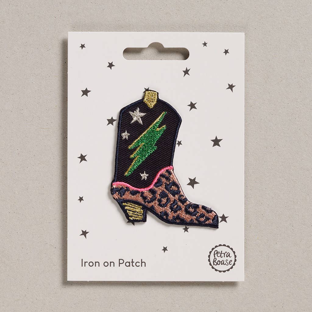 an embroidered cowboy boot which fashions black and peach leopard print at the toe with a golden heel. The rest of the boot is black with a green bolt and silver stars with golden loop on top. The background is white with black stars.