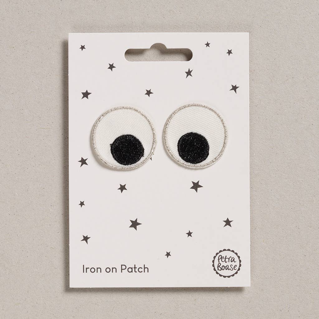 an embroidered googly eyes patch mainly white with black pupils and silver trim. The background is white with black stars.