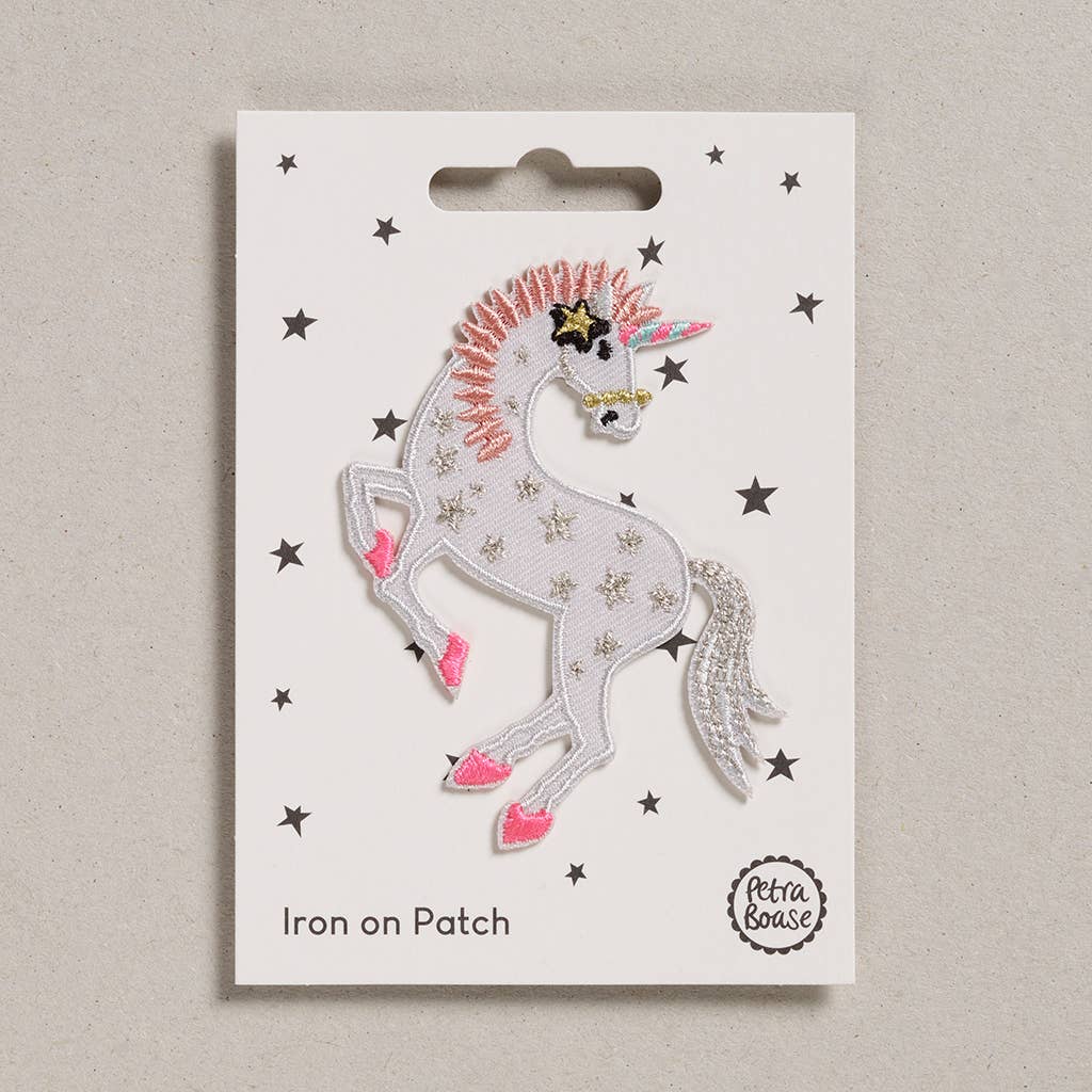 an embroidered unicorn. The unicorn is white in colour with silver tail and pink mane. Her feet are pink and her body is adorned with silver stars. She has a black and pink star near her ear. Her horn is pink and blue. The background is white with black stars